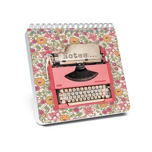 May include: A spiral-bound notepad with a floral pattern featuring pink, yellow, and green flowers. The notepad has a pink typewriter graphic with the word "Notes..." printed on the paper.