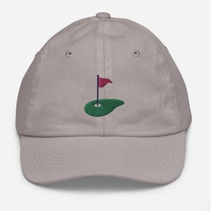 May include: A gray baseball cap with an embroidered green golf course and a red flag.