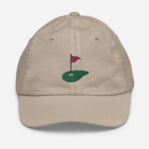May include: A beige baseball cap with an embroidered green golf green and a red flag.