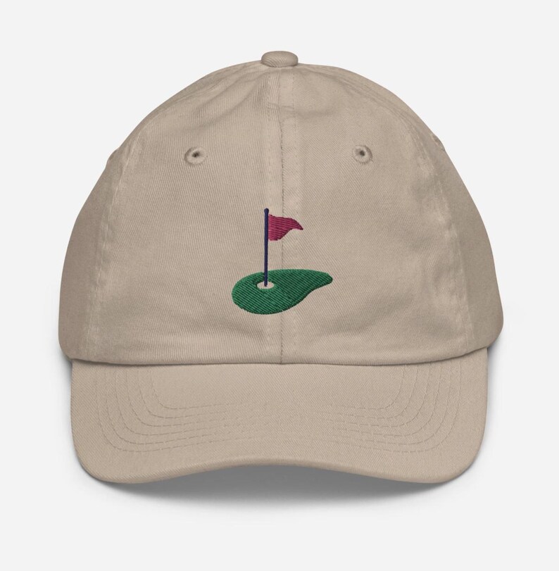 May include: A beige baseball cap with an embroidered green golf green and a red flag.
