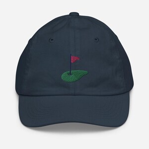 May include: A navy blue baseball cap with an embroidered green golf course and red flag.