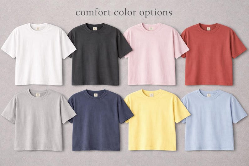 Puede incluir: Ocho camisetas de manga corta en varios colores: blanco, negro, rosa, rojo, gris, azul marino, amarillo y azul claro. El texto "comfort color options" se muestra en la parte superior.