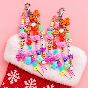 May include: Two colorful beaded bag charms featuring silver lobster clasps, orange bows, and various plastic beads including stars, hearts, flowers, and cat faces. One charm features the name LAUREL and the other features the name SOPHIA.