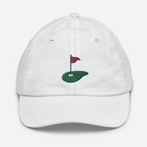 May include: White baseball cap with an embroidered green golf course and a red flag.