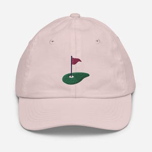 May include: A pink baseball cap with an embroidered green golf course and a red flag.