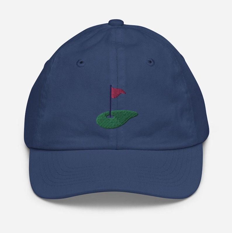 May include: A navy blue baseball cap with an embroidered green golf course and a red flag.
