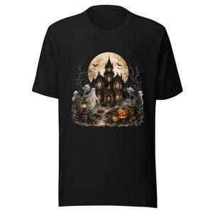 May include: A black short-sleeve t-shirt featuring a graphic print of a haunted mansion under a large full moon. The scene includes a white ghost, bare trees, two orange jack-o'-lanterns, and flying bats, all rendered in a dark, atmospheric style.