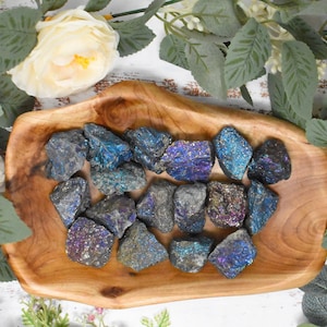 May include: A collection of iridescent pyrite crystals in various sizes and shapes, displayed in a wooden bowl. The crystals have a metallic sheen with shades of blue, purple, and gold.