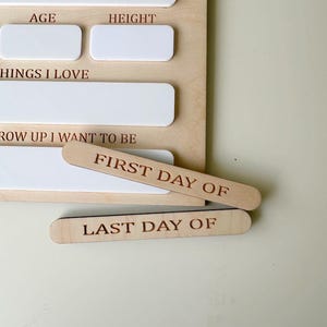 May include: Wooden growth chart with white spaces to fill in age, height, favorite things, and what they want to be when they grow up.  The chart also includes two wooden pieces that say "First Day Of" and "Last Day Of".