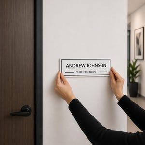 May include: A rectangular white office door sign with a black border and black text that reads ANDREW JOHNSON and CHIEF EXECUTIVE, featuring horizontal lines above and below the job title, held against a light-colored wall.