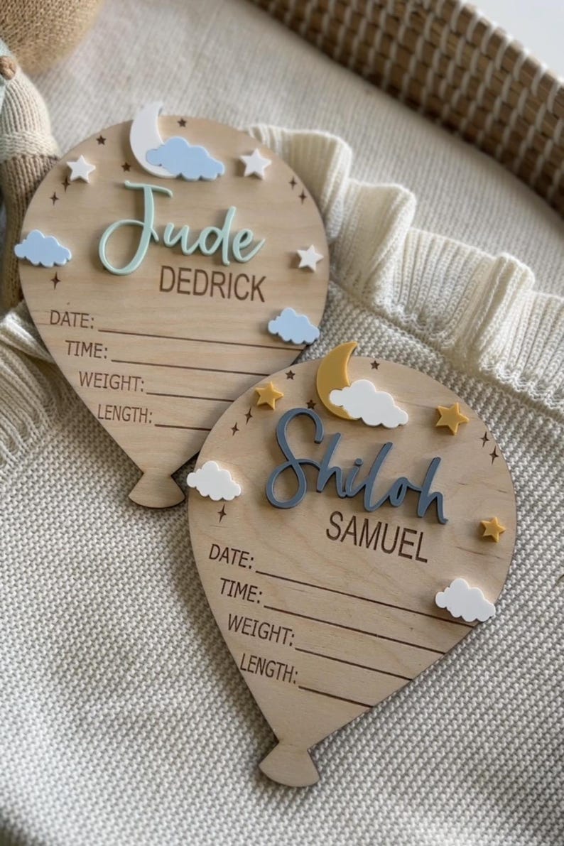 Pode incluir: Duas placas de madeira em forma de bal&atilde;o para anunciar o nascimento de um beb&eacute;. Uma diz "Jude Dedrick" com uma lua, nuvens e estrelas. A outra diz "Shiloh Samuel" com uma lua, nuvens e estrelas. Cada uma tem linhas para data, hora, peso e comprimento.