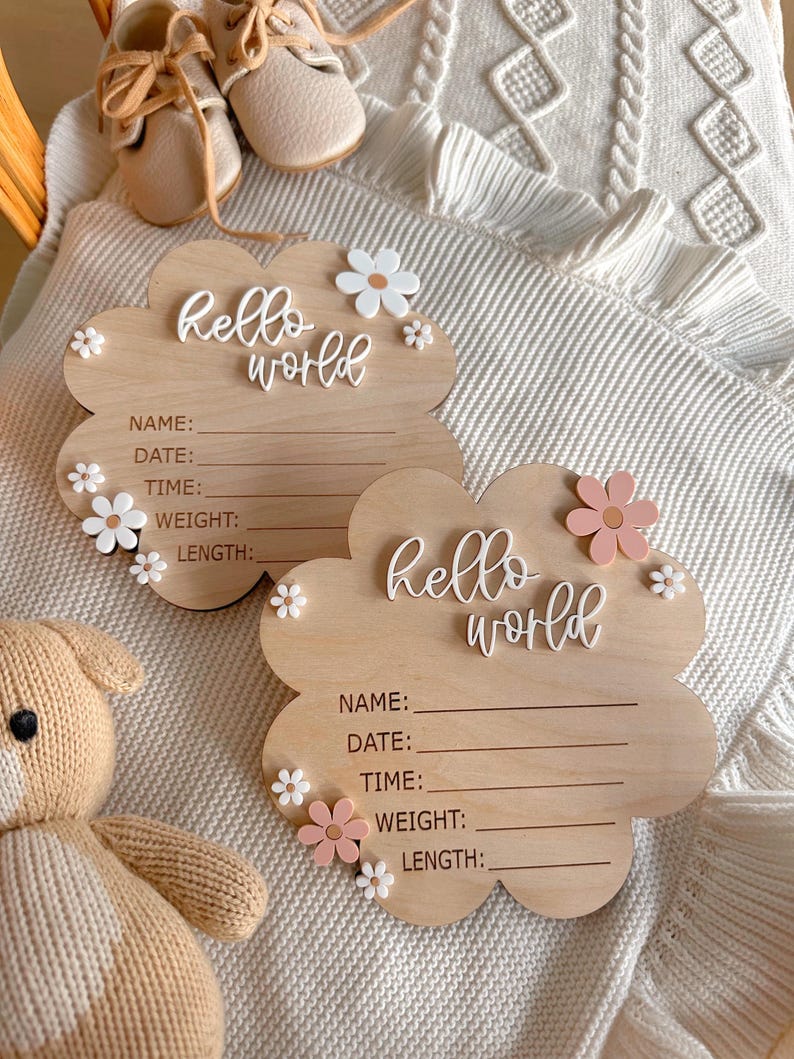 May include: Two wooden cloud-shaped signs with the text "hello world" and blank spaces for name, date, time, weight, and length. The signs are decorated with white and pink flowers.
