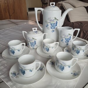 May include: A white porcelain tea set with a grape motif. The set includes a teapot, creamer, sugar bowl, and four cups and saucers.