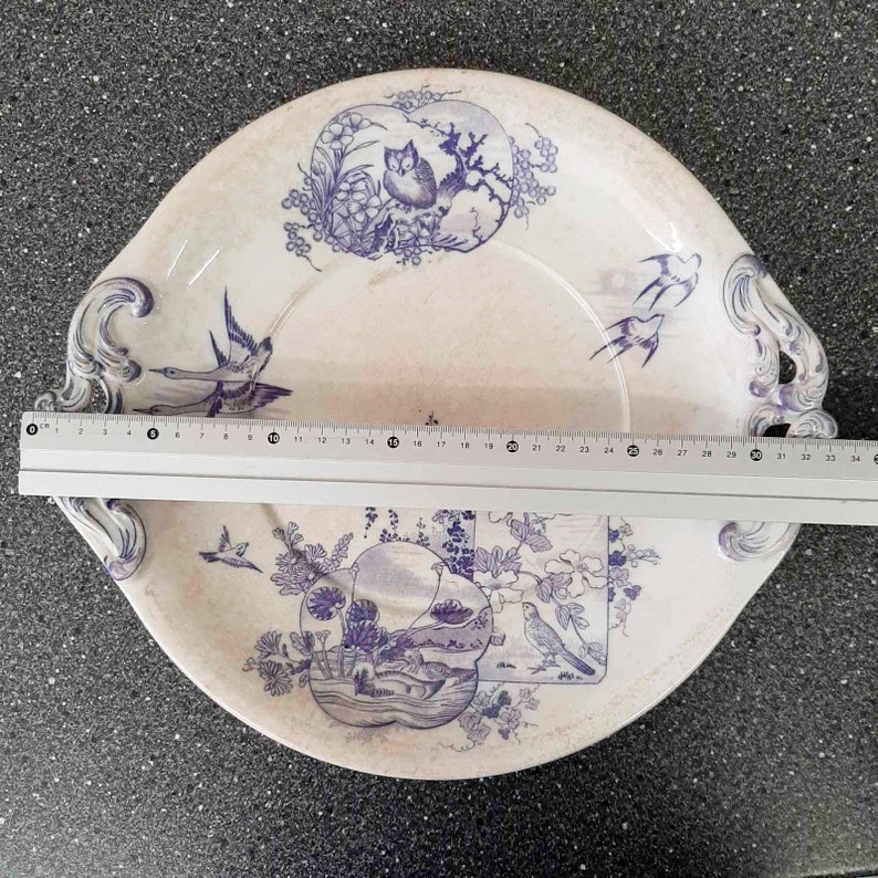 Puede incluir: Un plato de servir de cer&aacute;mica blanca con dise&ntilde;os florales y de p&aacute;jaros azules. El plato tiene dos asas y un borde elevado.