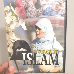 May include: DVD case with the title "Women in Islam." The cover shows a group of women in headscarves, with a woman in a light blue head covering holding a volleyball. White flowers are on the left side of the case.