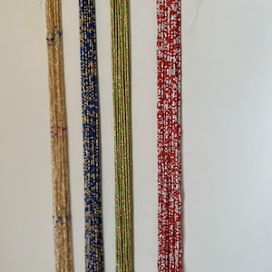 May include: Four strands of beaded jewelry, each with a different color and pattern. The strands are hanging from a white wall. The strands are beige, blue, green, and red.