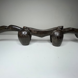 May include: A dark brown wooden sculpture of a stylized animal with a long, curved neck and a rounded body. The sculpture is carved with intricate details and has a smooth, polished finish.
