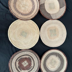 Puede incluir: Seis cestas redondas tejidas con varios patrones y colores. Las cestas tienen tonos marrones, beige y crema, con diseños intrincados. Los bordes son de color marrón oscuro. Las cestas están dispuestas sobre una superficie negra.