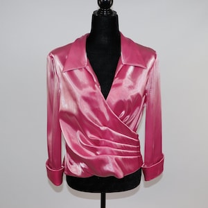 May include: A pink satin wrap blouse with a v-neck and long sleeves. The blouse has a gathered detail at the waist.