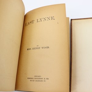 May include: An open book with the title "East Lynne" by Mrs. Henry Wood. The book was published by Donohue, Henneberry & Co. in Chicago.