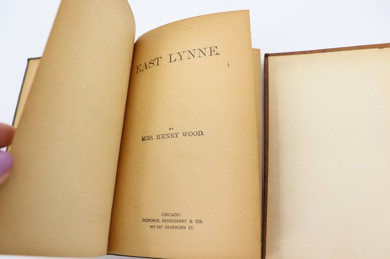 May include: An open book with the title "East Lynne" by Mrs. Henry Wood. The book was published by Donohue, Henneberry & Co. in Chicago.