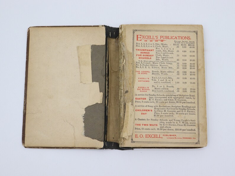May include: A vintage book with a red and black cover. The cover features the title "Excell's Publications" and a list of publications with prices. The book is open to a page with a price list for various publications, including "Triumphant Songs for Sunday Schools", "The Gospel in Song", "Excell's Anthems", "Easter Service", "Children's Day", and "The Two Ways".