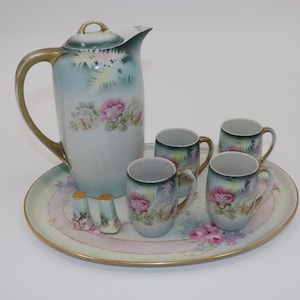 May include: A vintage porcelain tea set with a floral design. The set includes a teapot, four cups, a tray, and two salt and pepper shakers.