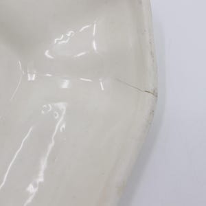 May include: White ceramic bowl with a scalloped edge. The bowl has a small crack on the side.
