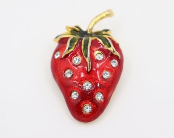 May include: A red enamel strawberry brooch with gold trim and clear rhinestones.