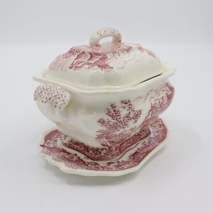 May include: A white porcelain soup tureen with a pink floral design. The tureen has a lid and a matching base.