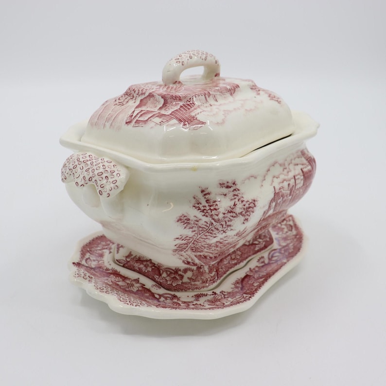 May include: A white porcelain soup tureen with a pink floral design. The tureen has a lid and a matching base.