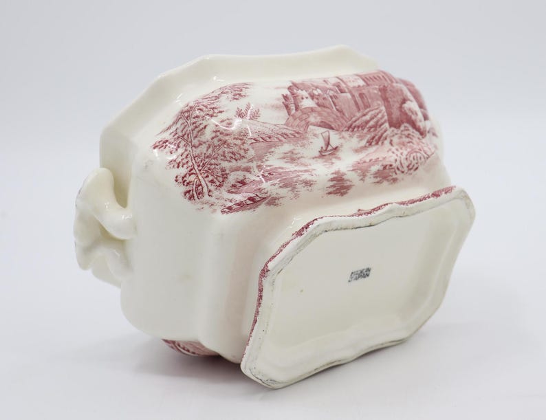May include: White ceramic serving dish with a pink floral pattern and a scalloped edge. The dish has two handles and a raised base. The bottom of the dish has a stamp that reads "England".