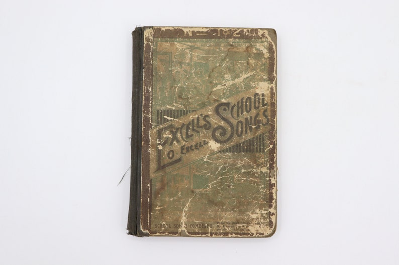 May include: A vintage book titled "Excel's School Songs" with a worn, green cover and brown spine. The book is slightly damaged and has a frayed edge.