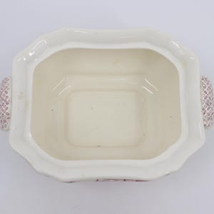 May include: White ceramic serving dish with a square shape and two handles. The handles are decorated with a pink and white pattern. The dish has a scalloped edge.