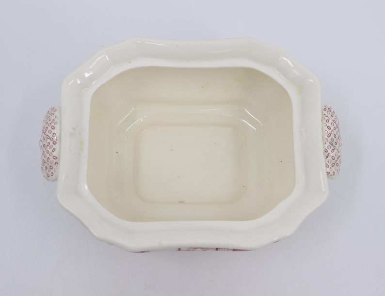 May include: White ceramic serving dish with a square shape and two handles. The handles are decorated with a pink and white pattern. The dish has a scalloped edge.