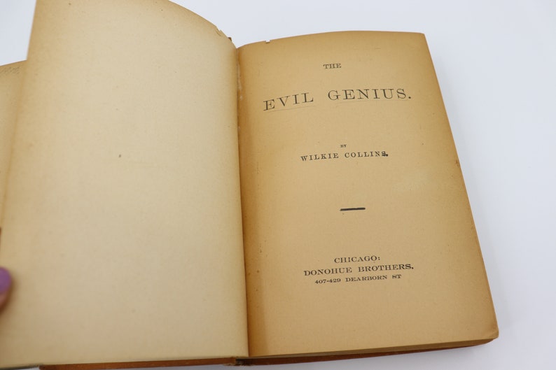 May include: The cover of a vintage book titled "The Evil Genius" by Wilkie Collins. The book was published by Donohue Brothers in Chicago.