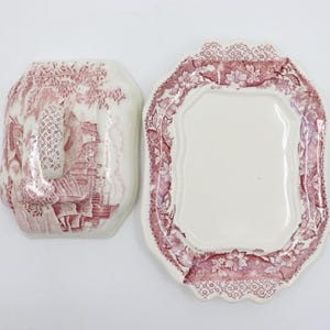 May include: A vintage white ceramic butter dish with a red floral pattern. The dish has a lid with a handle and a scalloped edge.