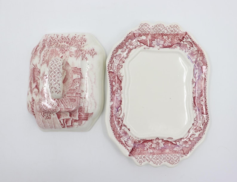 May include: A vintage white ceramic butter dish with a red floral pattern. The dish has a lid with a handle and a scalloped edge.