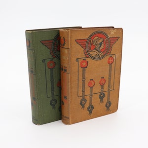May include: Two vintage hardcover books with green and brown covers. The book on the right has the title "The Trail of Genius" and features a decorative design with a woman's head in a crown and red stars.