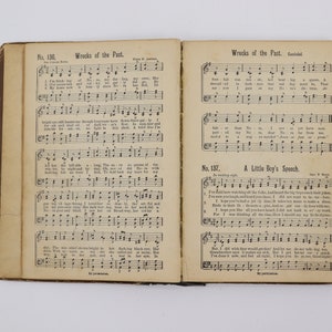 May include: An open book with sheet music for two songs, "Wrecks of the Past" and "A Little Boy's Speech". The music is printed in black ink on white paper. The book is bound in brown leather.