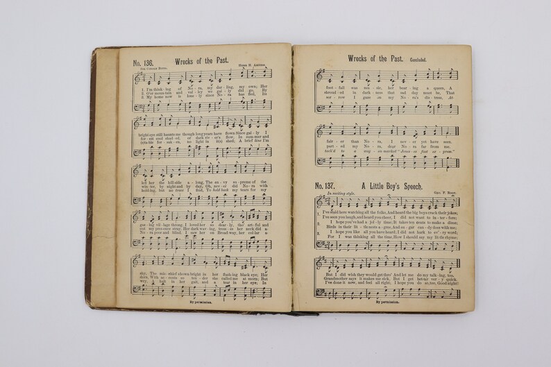 May include: An open book with sheet music for two songs, "Wrecks of the Past" and "A Little Boy's Speech". The music is printed in black ink on white paper. The book is bound in brown leather.