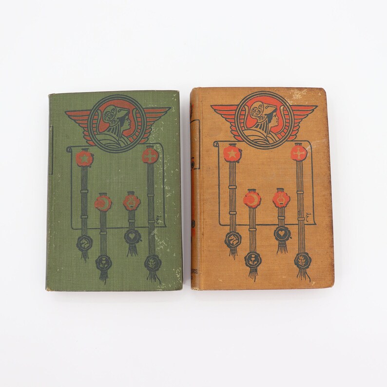 May include: Two vintage hardcover books with illustrated covers. The covers feature a woman in a crown with wings and a banner with stars. One book has a green cover and the other has a brown cover.