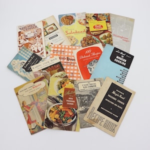 May include: A collection of vintage recipe books with colorful covers. Titles include "Kitchen Center," "Electric Cooking," "Saladmast," and "100 Delicious Recipes." The books feature illustrations of food and cooking appliances.