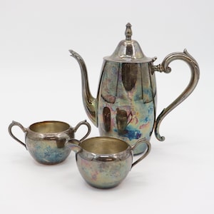May include: A silver-plated tea set comprising a teapot, creamer and sugar bowl. The set has a vintage look with a slightly iridescent finish.