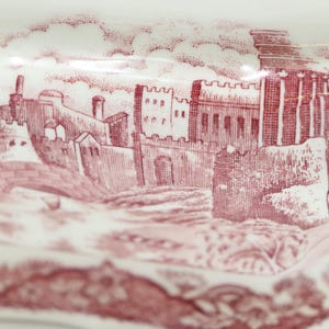 May include: A vintage ceramic dish with a red and white design featuring a detailed illustration of a castle.