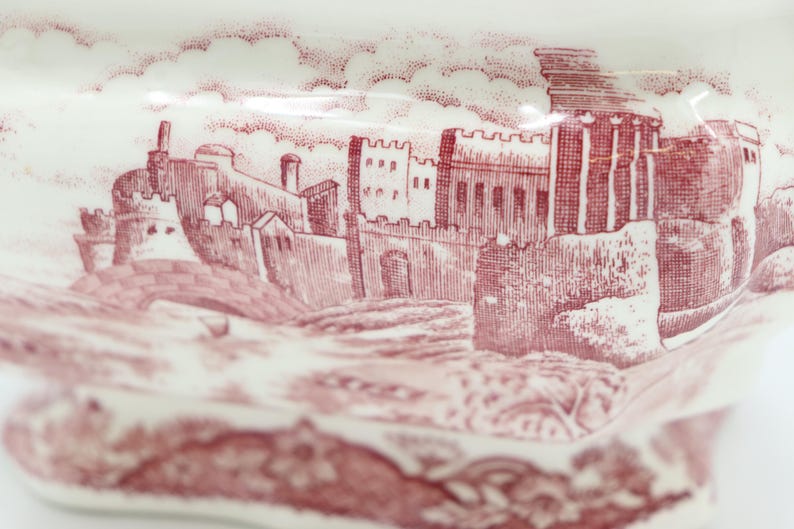 May include: A vintage ceramic dish with a red and white design featuring a detailed illustration of a castle.