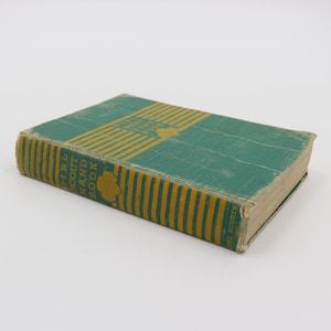 Peut inclure: Un livre vert et jaune avec le titre "Girl Scout Handbook" sur la couverture.