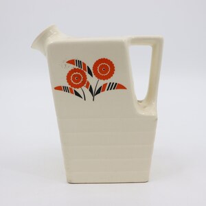 May include: A white ceramic jug with a handle and a floral design in orange and black. The jug has a rectangular body and a spout.