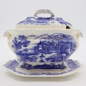 May include: A blue and white porcelain gravy boat with a lid and a matching base. The gravy boat features a scenic design of a castle and a river.