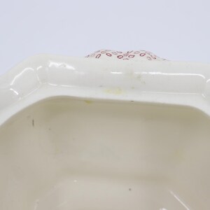 May include: White ceramic lidded jar with a red and white floral pattern. The lid is open and the inside of the jar is visible.